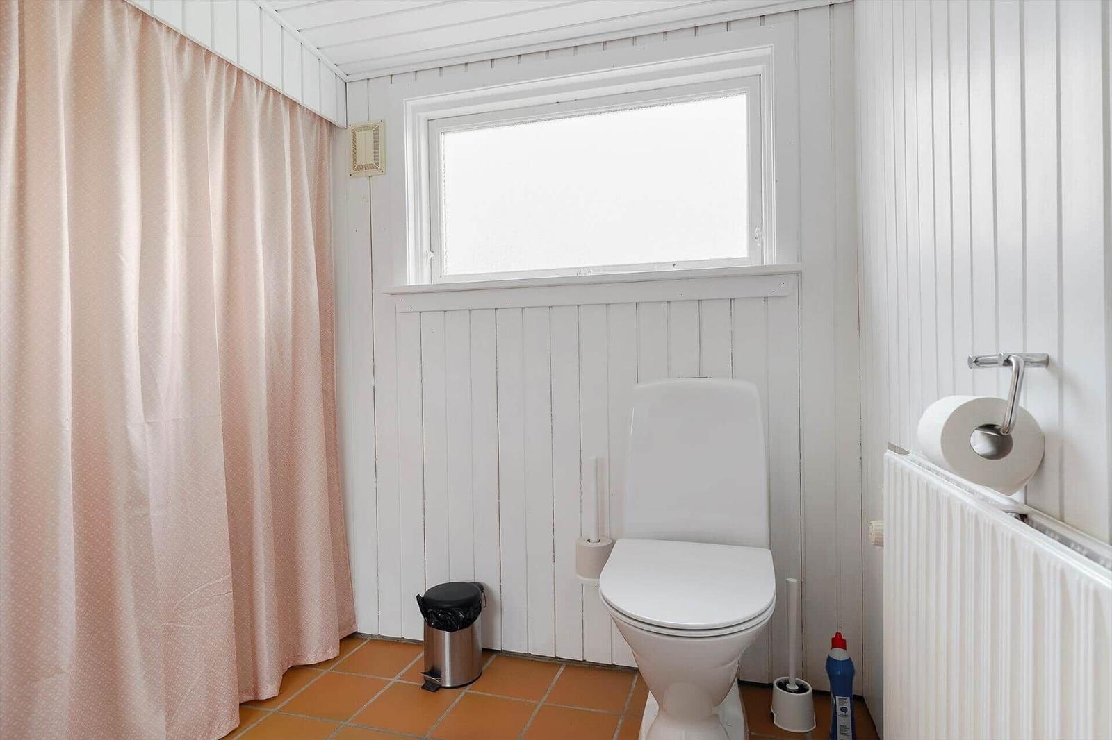 Badezimmer mit Toilette, Fenster und rosa Duschvorhang.