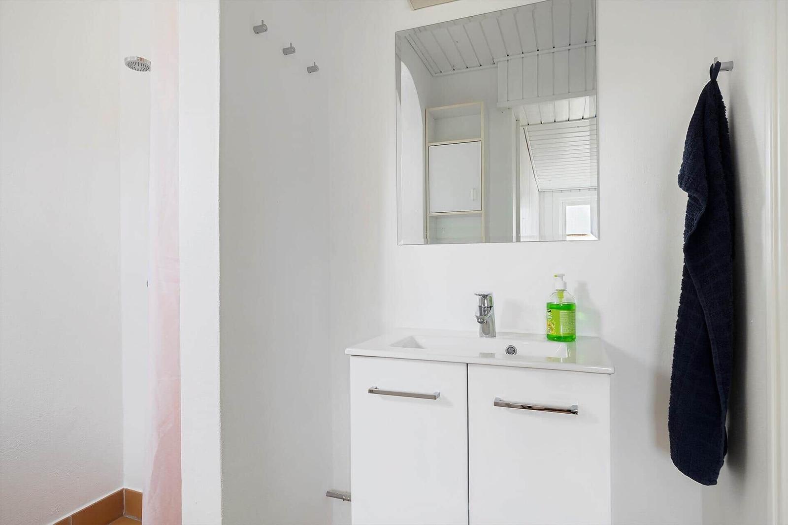 Badezimmer mit Waschbecken, Spiegel und Dusche. Handtuch hängt an Wand.