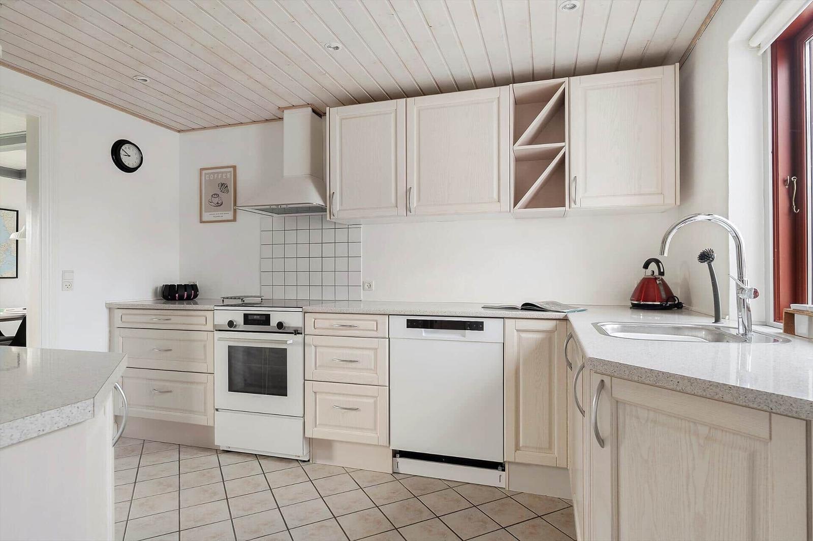 Küche mit hellen Schränken, Spüle und Backofen. Dachschrägen Decke und Fenster.