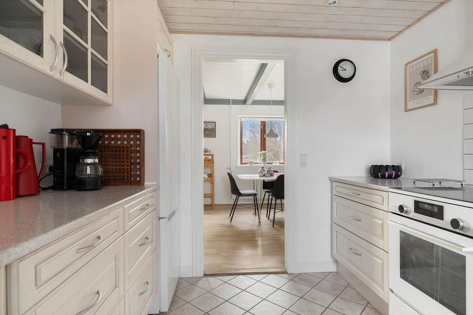 Küche mit Arbeitsfläche, Kühlschrank und Herd. Durchgang zur Essnische mit Tisch und Stühlen.