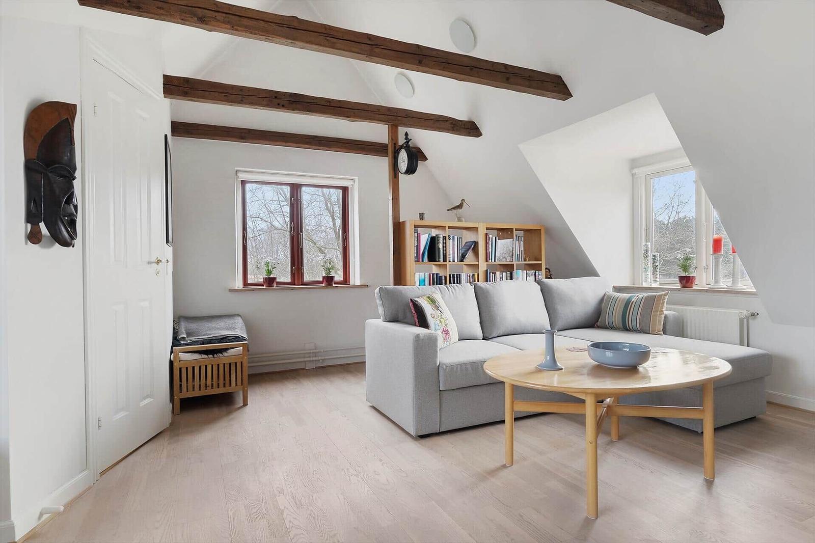 Wohnzimmer mit grauem Sofa, Holztisch und Bücherregal unter Dachschrägen.