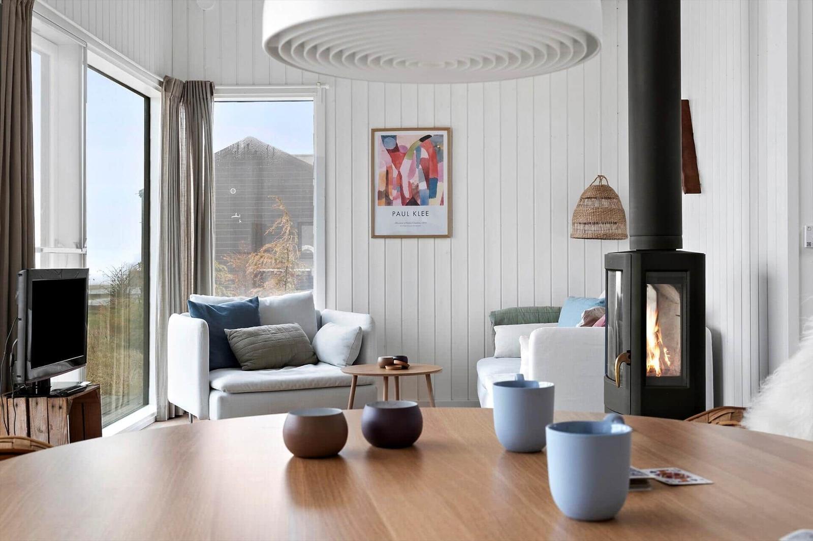 Wohnraum mit Kamin, Sofa und großem Fenster. Tisch mit Tassen und Deko.