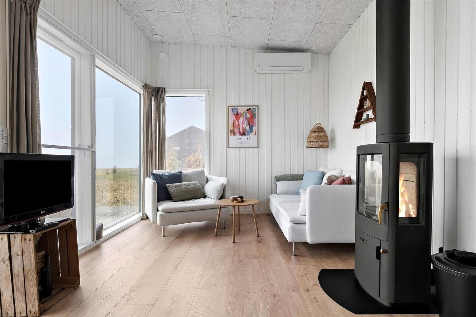 Wohnraum mit Kamin, Sofa und Fernseher. Große Fenster mit Blick auf die Landschaft.