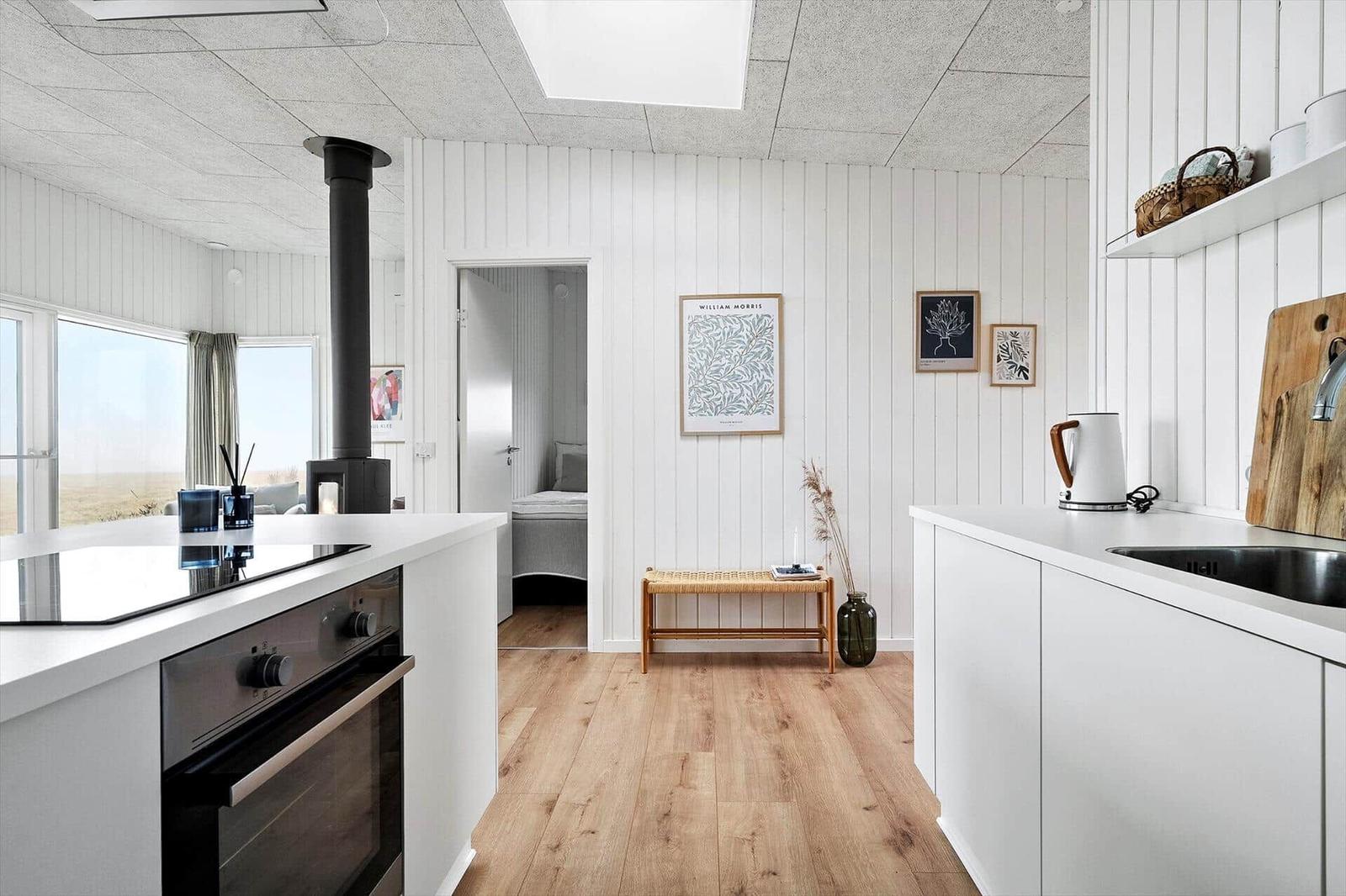 Küche mit Holzboden, weißen Schränken und Blick in Schlafzimmer