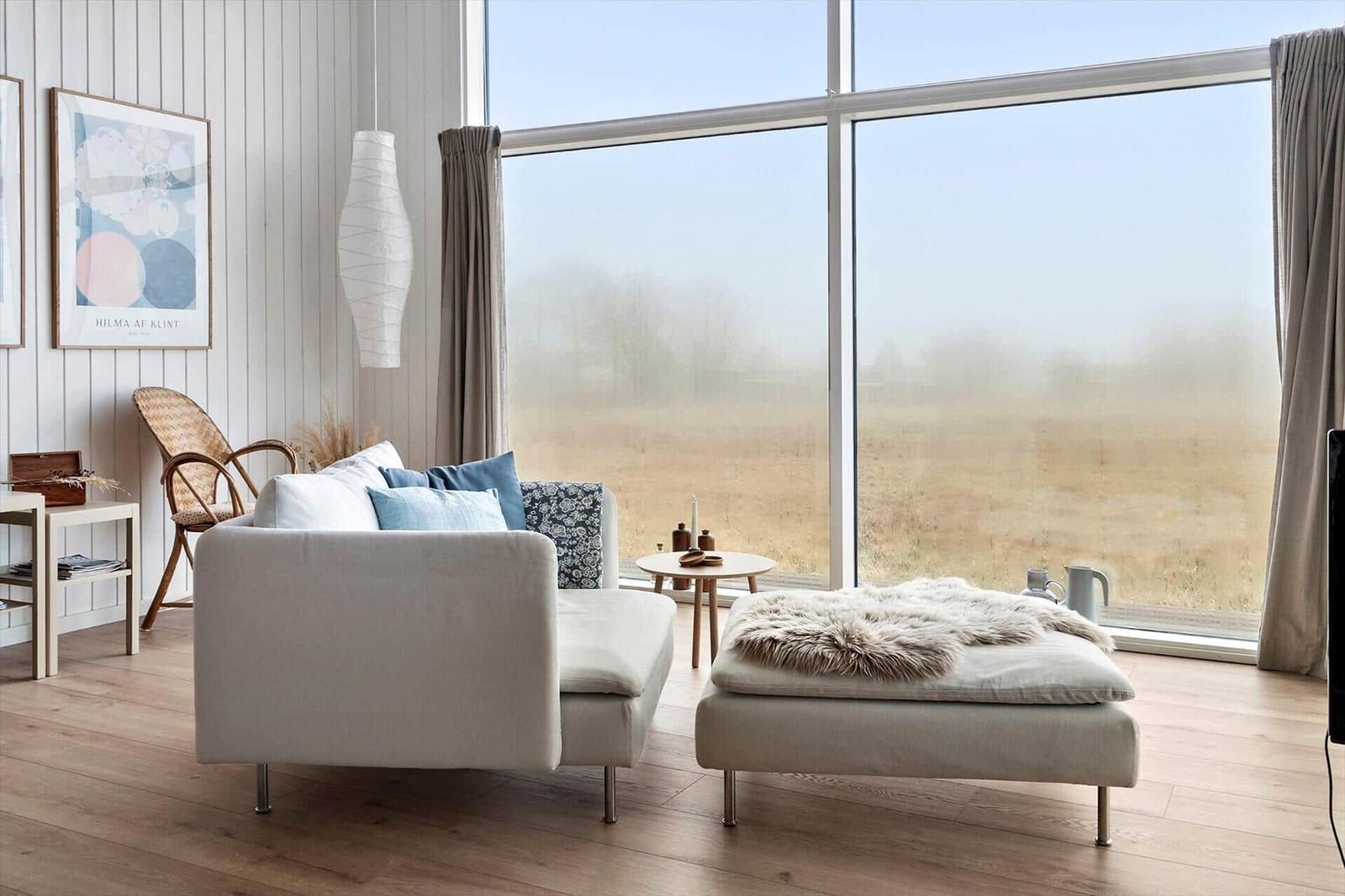 Wohnzimmer mit Sofa, Sitzbank und großem Fenster zur Landschaft.