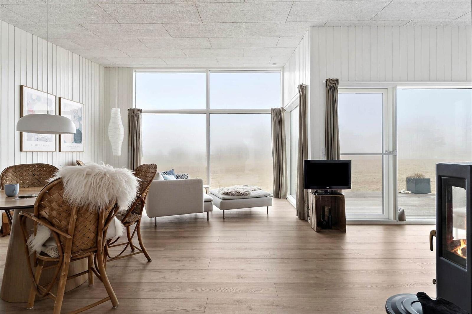 Wohnzimmer mit großem Fenster, Holzboden und Kamin. Möbel sind modern und schlicht.