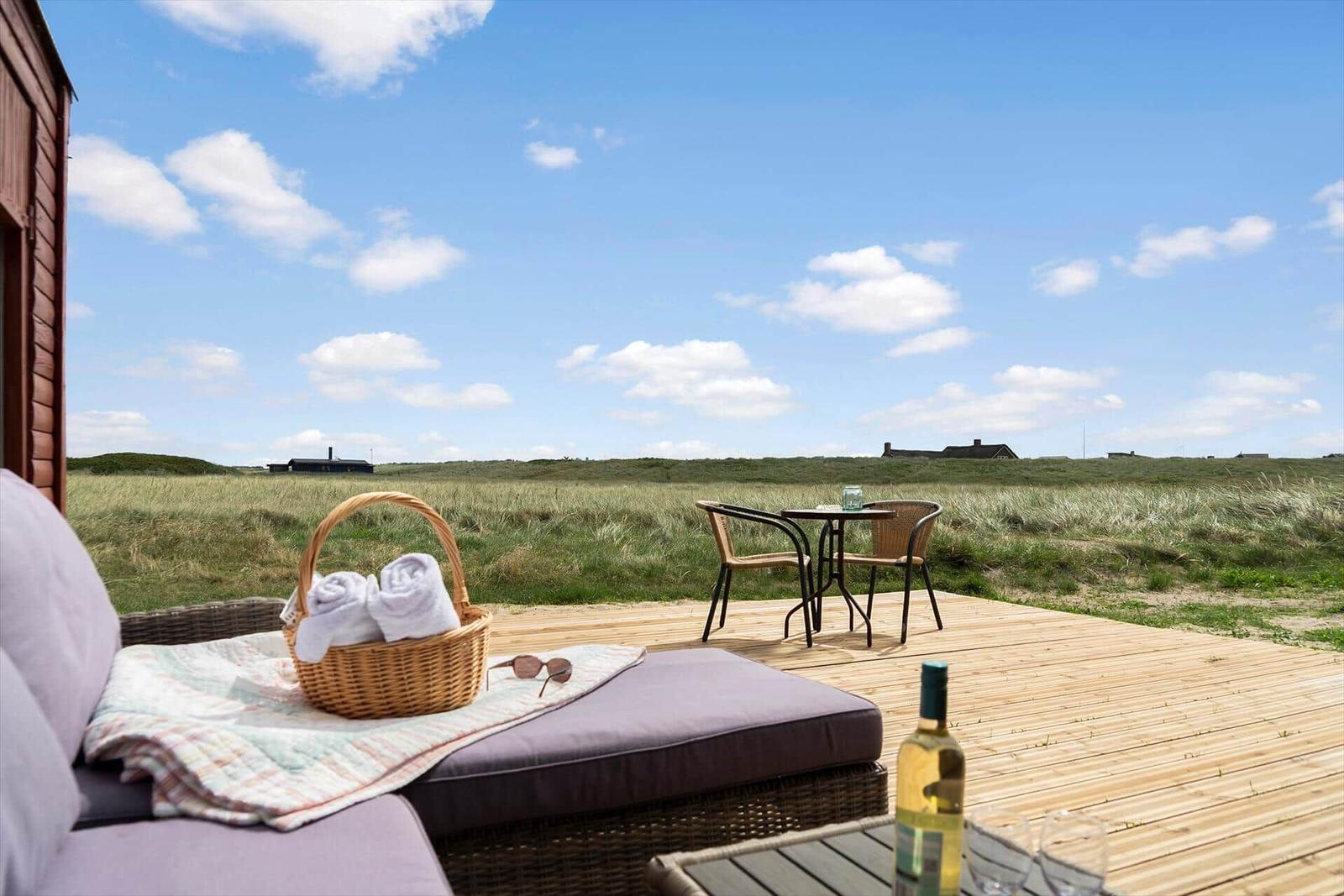 Terrasse mit Liege, Tisch und Stühlen, Blick auf Grasland und Himmel.