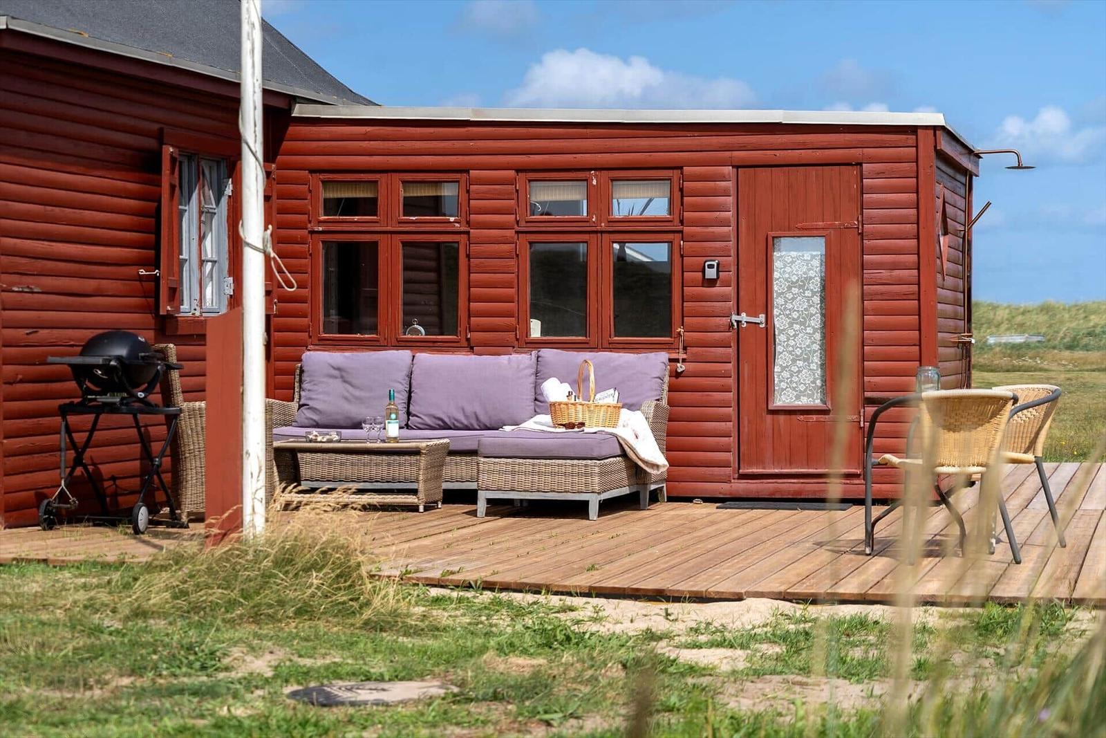 Roter Holzhaus mit Terrasse, Sofa, Grill und Sitzgelegenheiten.