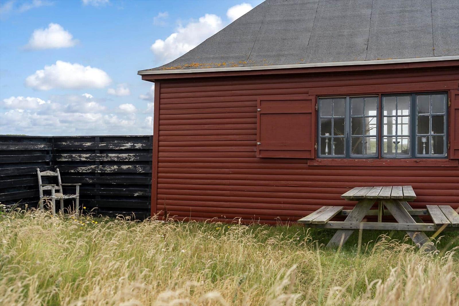Rotes Holzhaus mit Picknicktisch und Stuhl im Gras. Fenster mit Glasteilen.