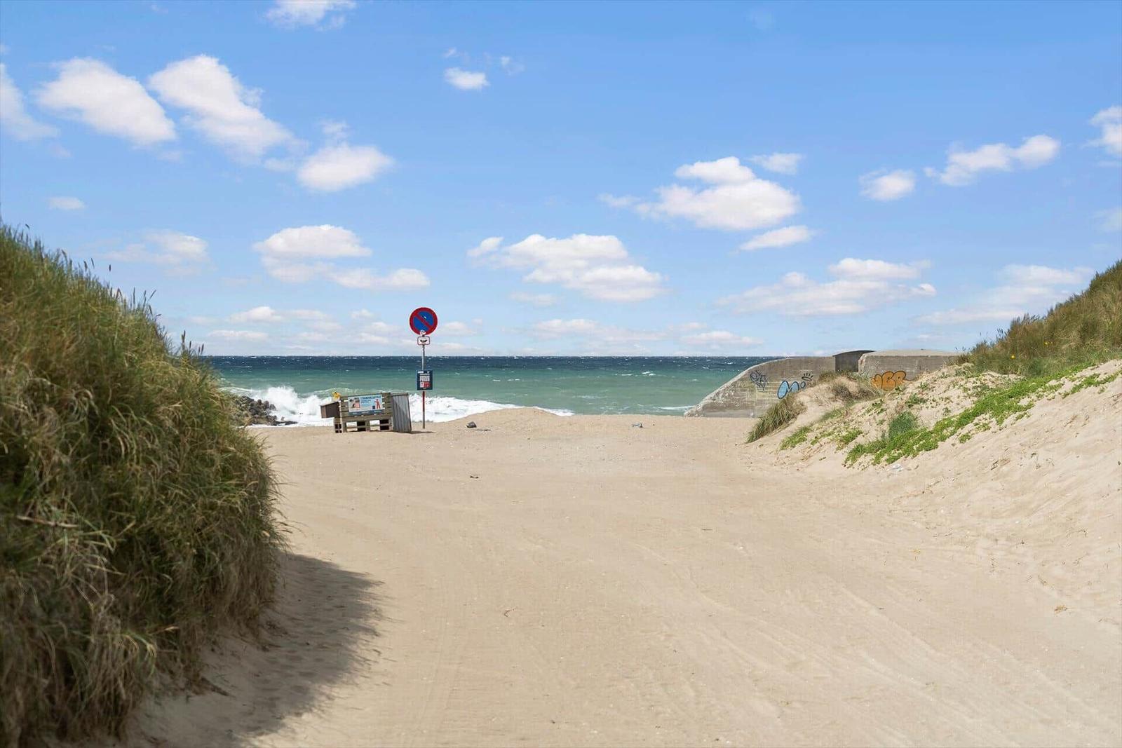 Sandweg führt zum Strand mit Blick auf das Meer und einen Verkehrszeichenpfosten.