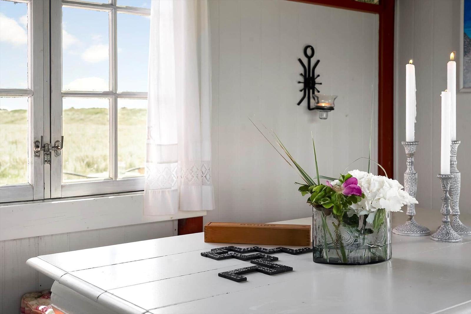 Tisch mit Blumen, Kerzen und Dominosteine vor Fenster mit Blick auf Grasland.