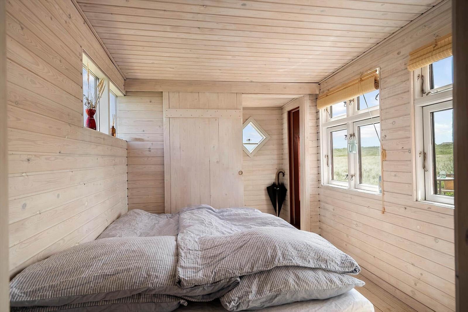 Schlafzimmer mit Holzwänden, Bett und Fenstern mit Blick.
