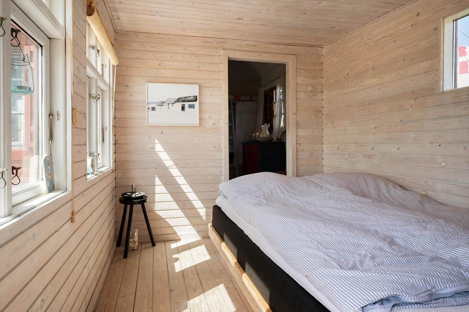 Schlafzimmer mit Holzwand und Bett. Fenster, Bild und Stuhl sind sichtbar.