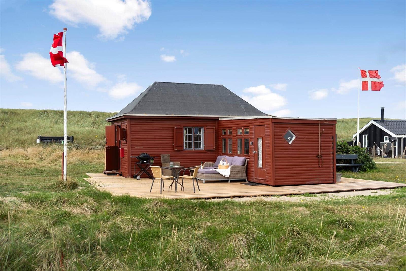 Rotes Holzhaus mit Terrasse, Grill und dänischer Flagge im Grasland.