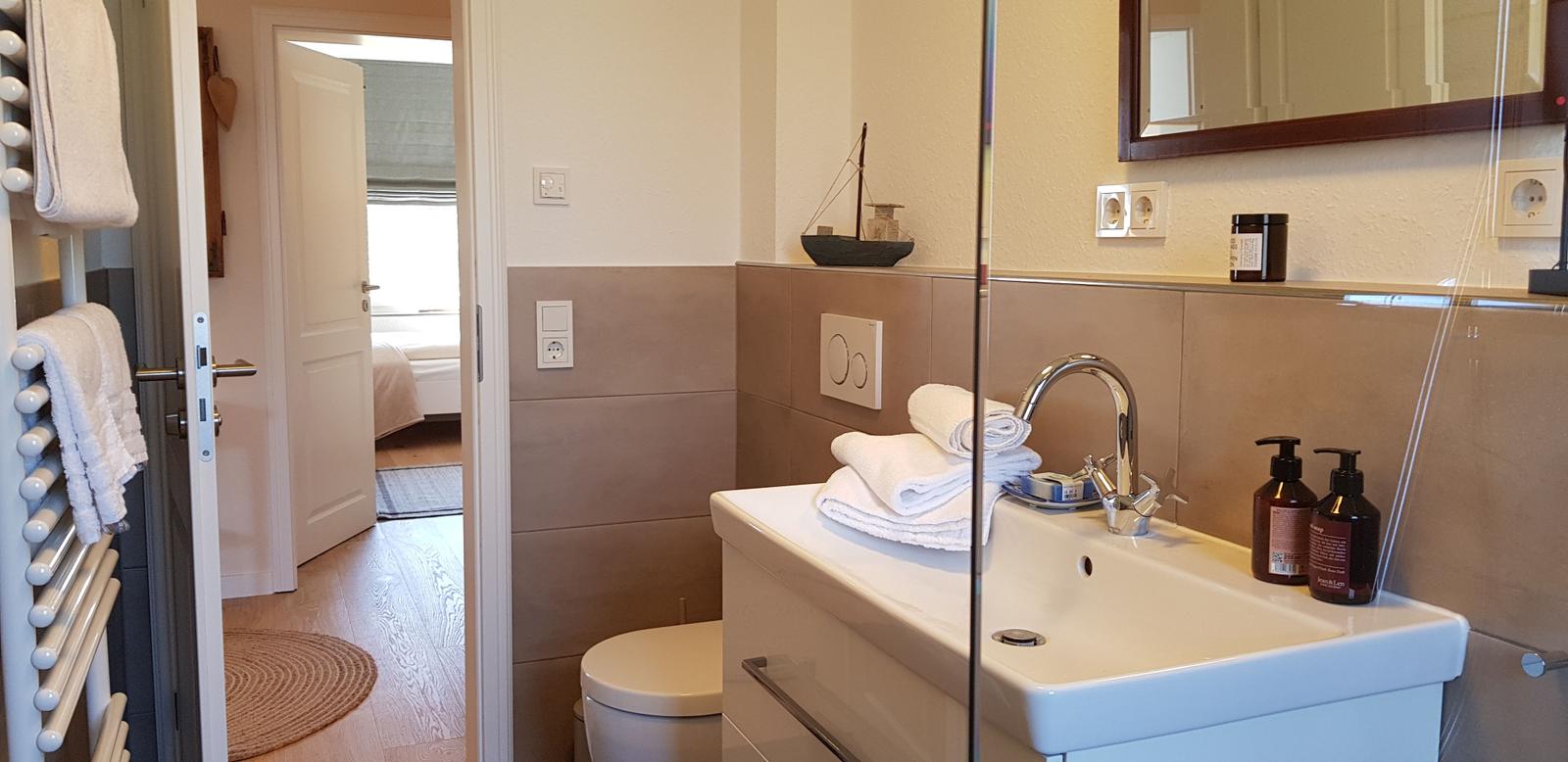 Badezimmer mit Waschbecken, Spiegel und Toilette. Handtücher und Seife sind vorhanden.