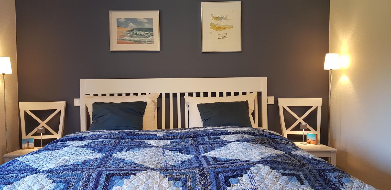 Schlafzimmer mit Bett, zwei Nachttischen und Wandbildern.