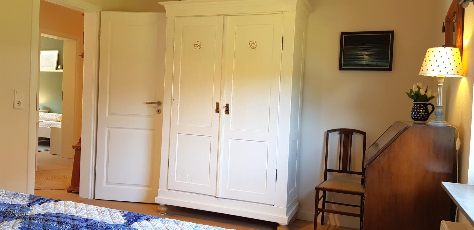 Schlafzimmer mit weißen Schrank, Holzstuhl und Lampen.