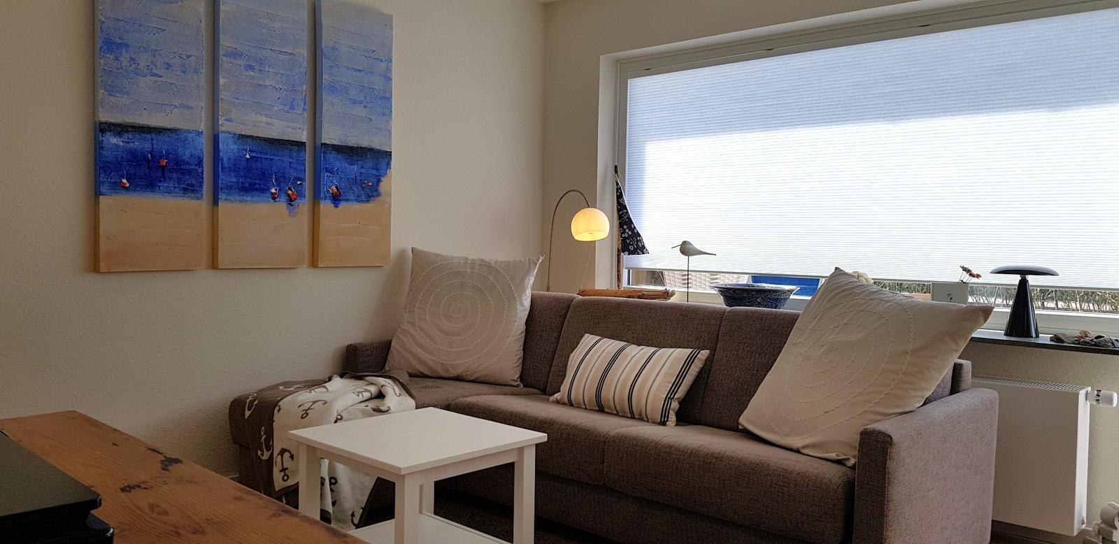 Wohnzimmer mit Sofa, Tisch und Wandbild. Fenster mit Jalousie.