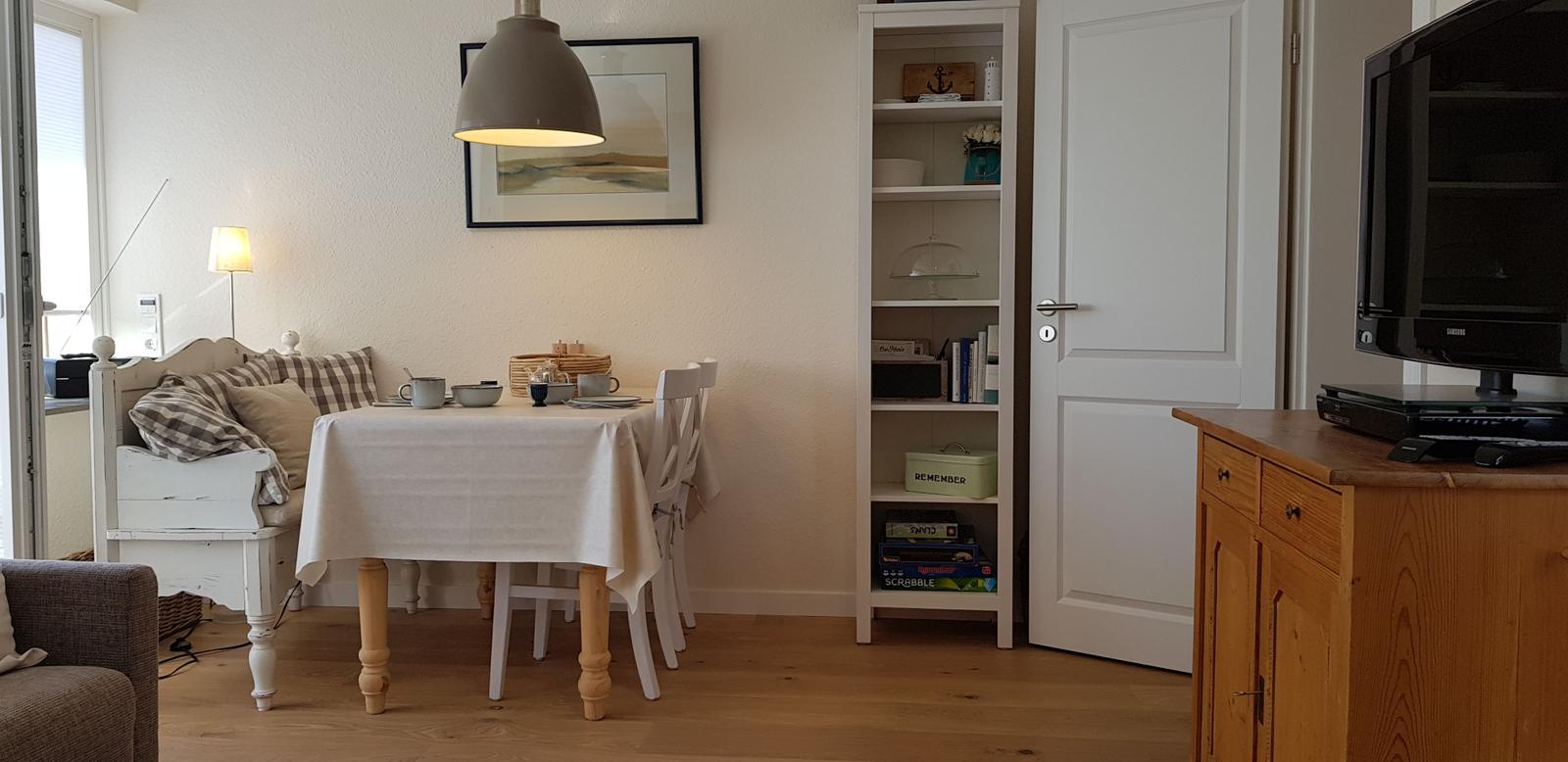 Essbereich mit Tisch, Stühlen und Bücherregal. Fernseher auf Holzschrank.