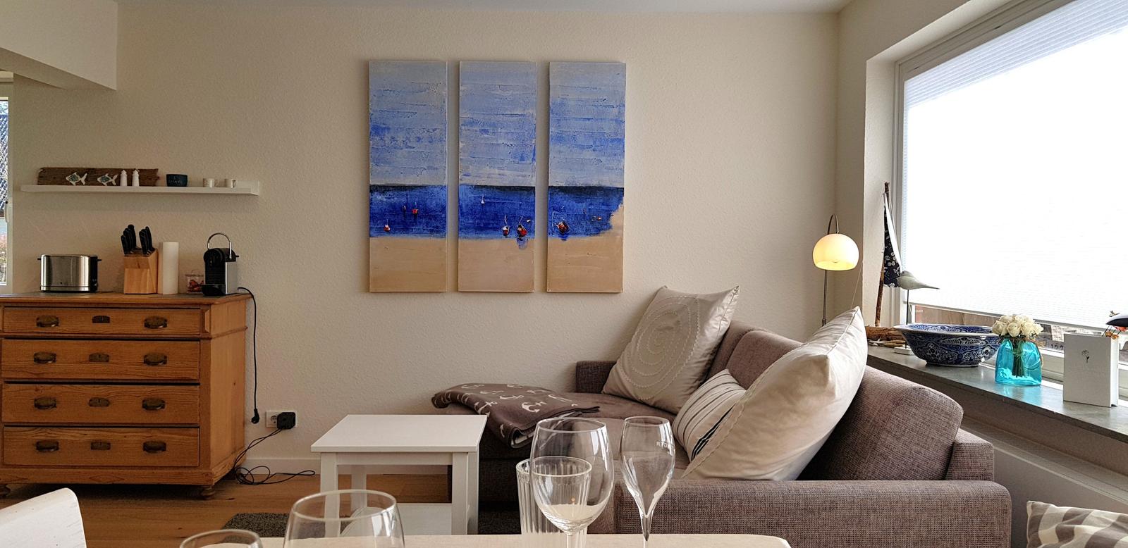 Wohnzimmer mit Sofa, Tisch und Wandbild. Fenster mit Blick nach draußen.