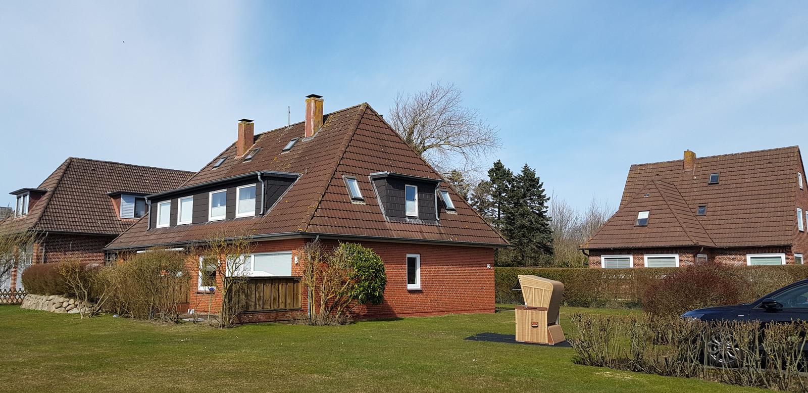 Ein zweistöckiges Haus mit rotem Dach und Garten. Ein Holzstuhl steht draußen.