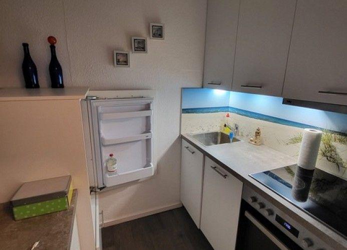 Küche mit Kühlschrank, Spüle und Herd. Oberflächen sind weiß. Wandbild mit blauem Licht.