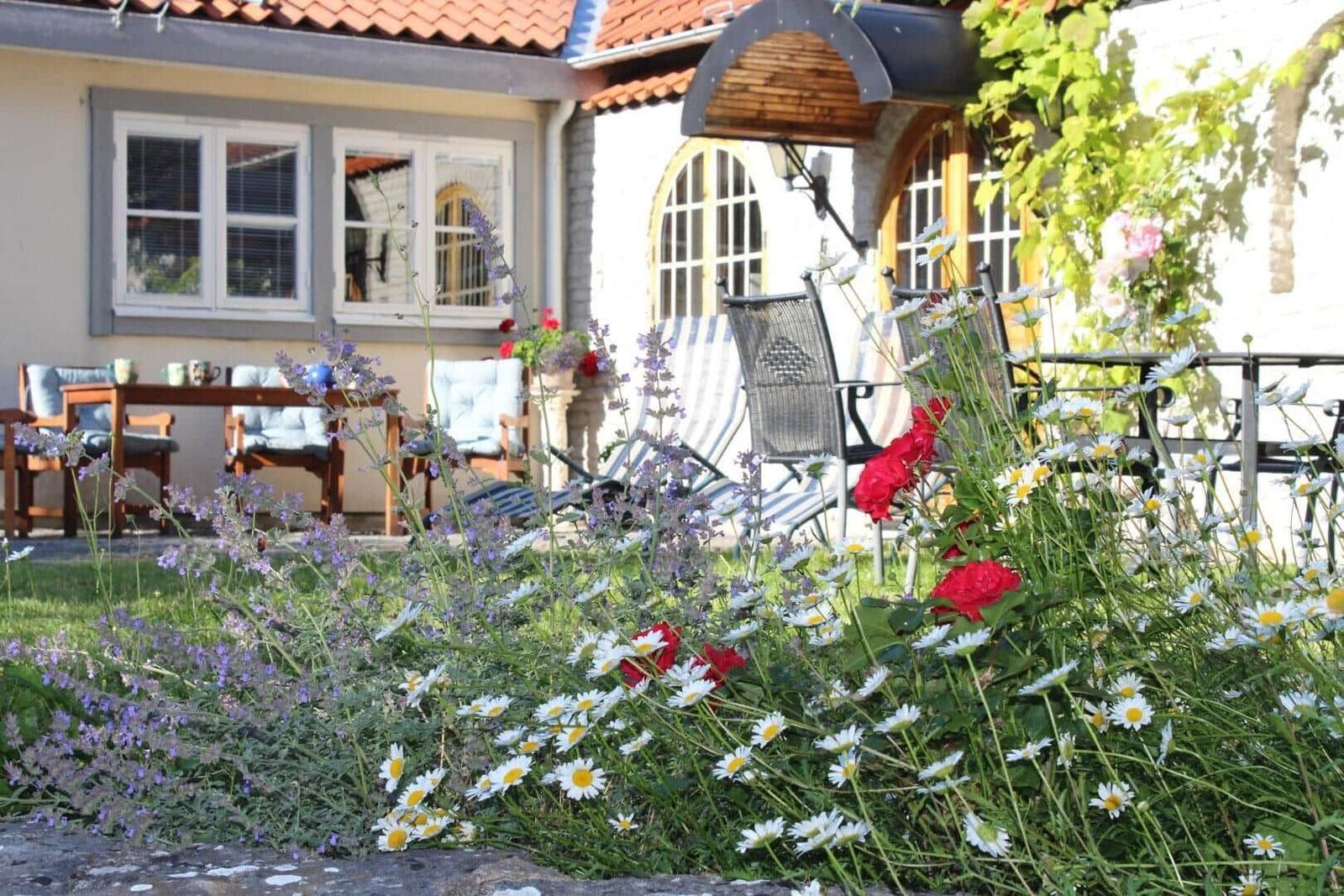 Garten mit Blumen und Sitzgelegenheiten vor einem Haus mit Terrasse.