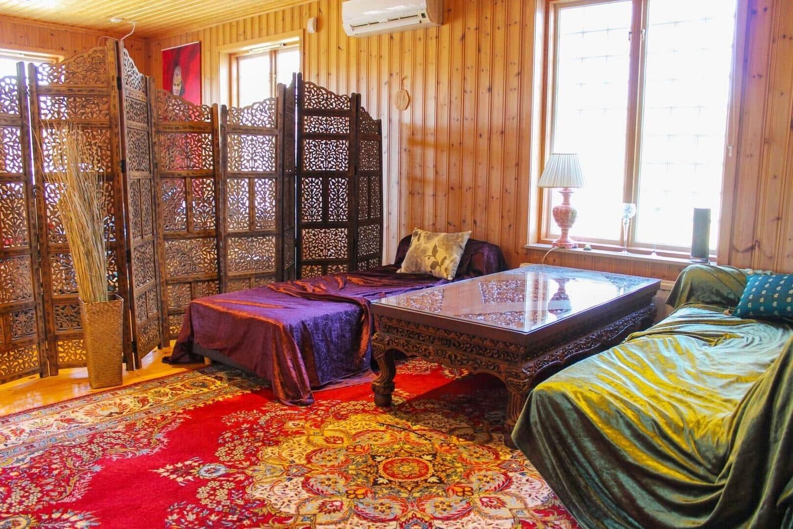 Zimmer mit Holzwand, Teppich, zwei Liegen und Tisch.