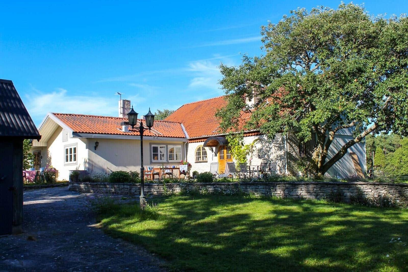 Haus mit rotem Dach, Garten und großer Baum. Terrasse mit Tisch und Stühlen.