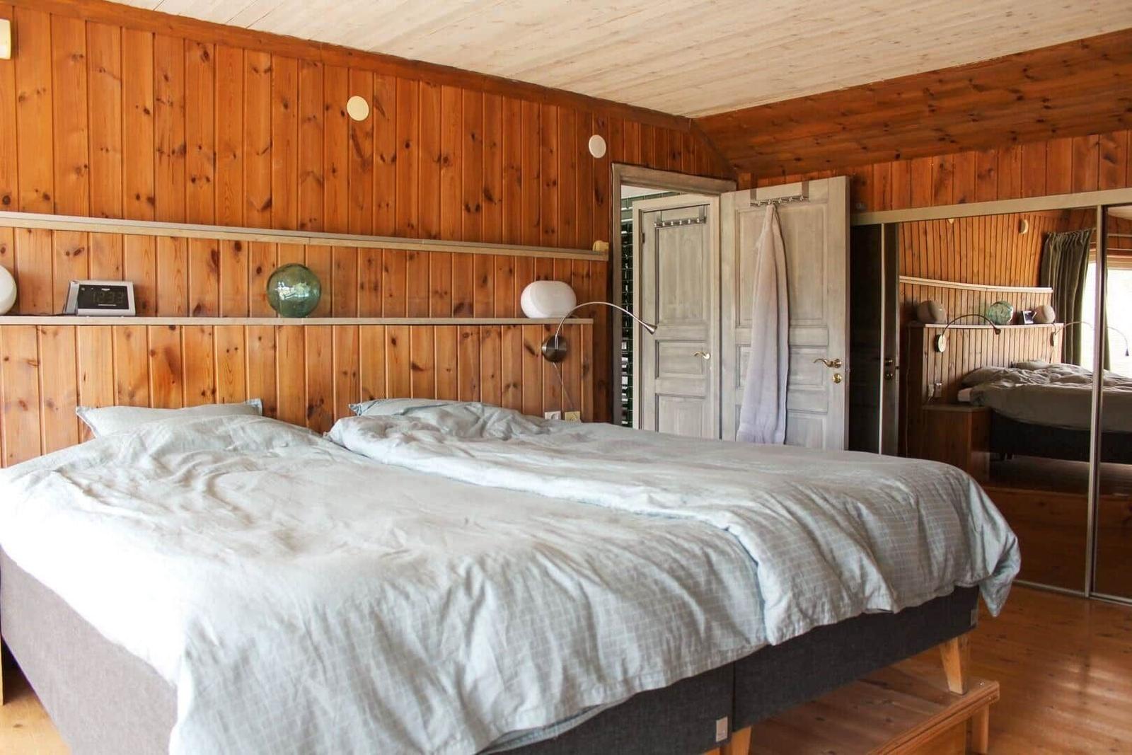 Doppelbett in einem Zimmer mit Holzwandverkleidung und Spiegelschrank.