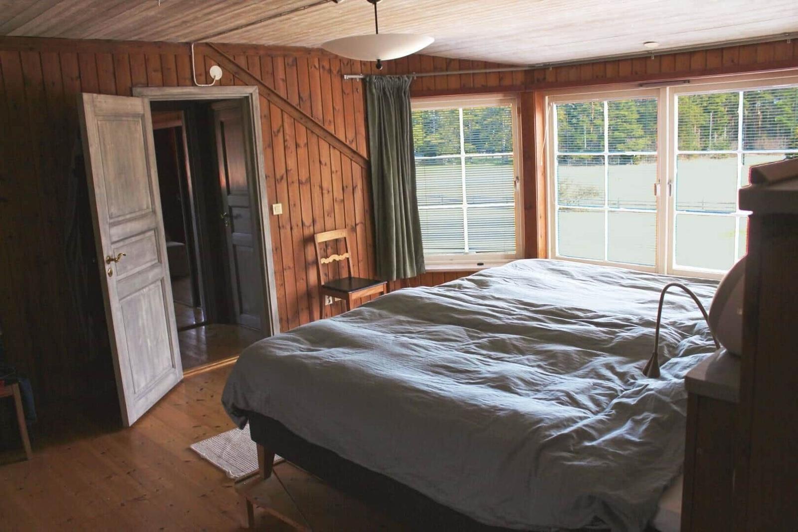 Schlafzimmer mit Bett, Fenstern und Holzwandverkleidung.