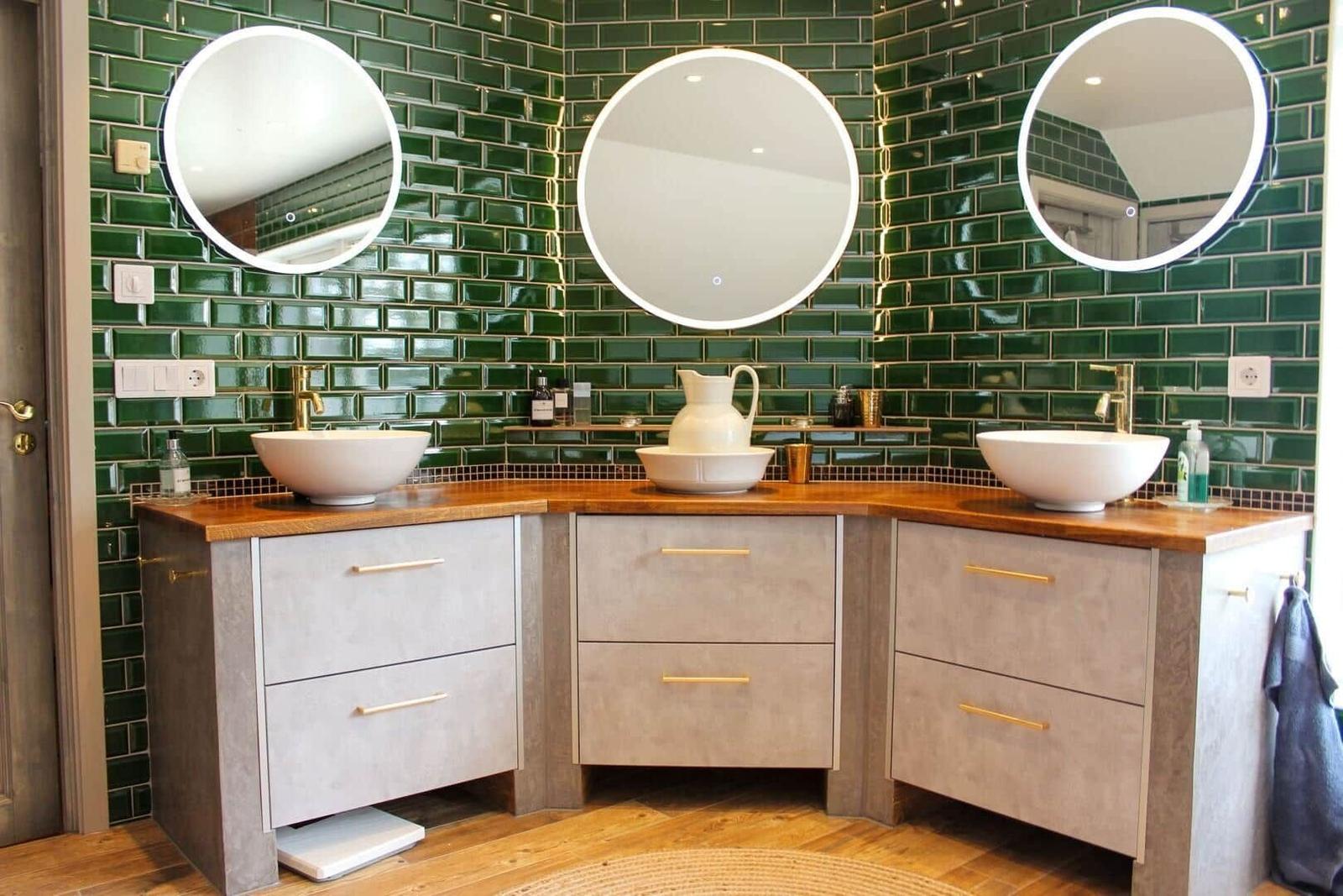 Dusche mit grünen Fliesen, drei runden Spiegeln und zwei Waschbecken auf Holzoberfläche.