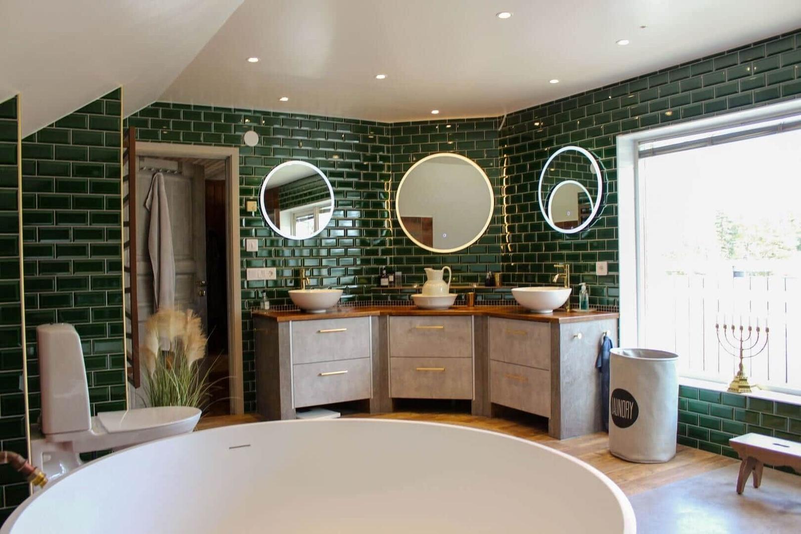 Badezimmer mit grünen Fliesen, drei Waschbecken und runden Spiegeln.