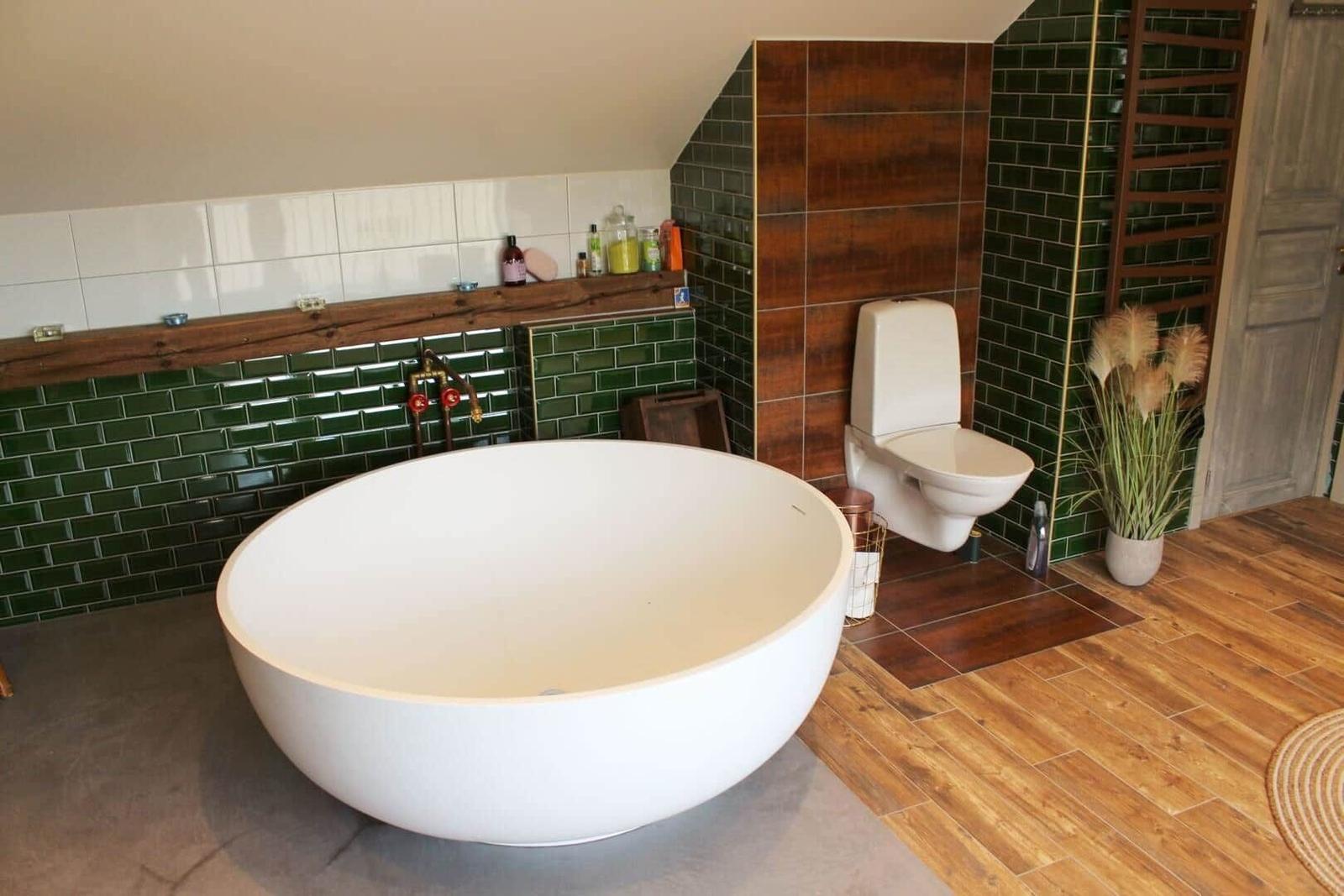 Bad mit freistehender Badewanne, Toilette und grünen Fliesen.