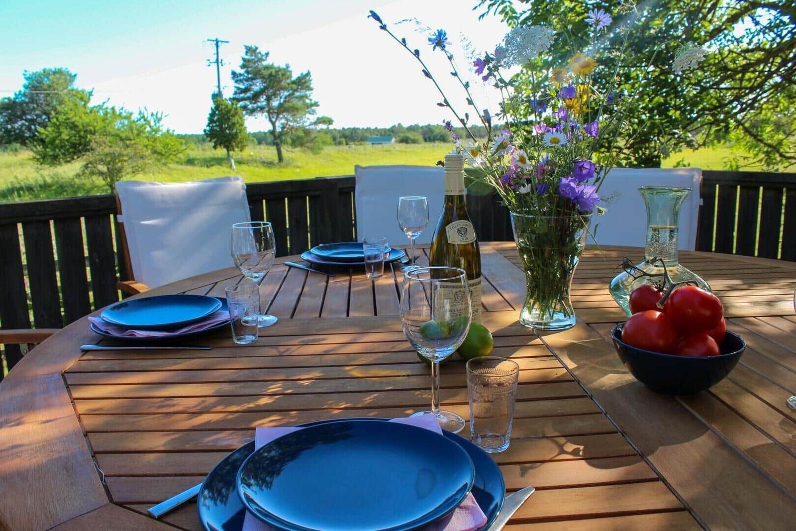 Rundtisch auf Terrasse mit Blumenvase, Weinflasche und Tomaten.