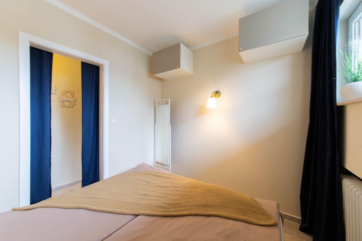 Schlafzimmer mit Bett, Wandlampe und Tür zum Badezimmer.