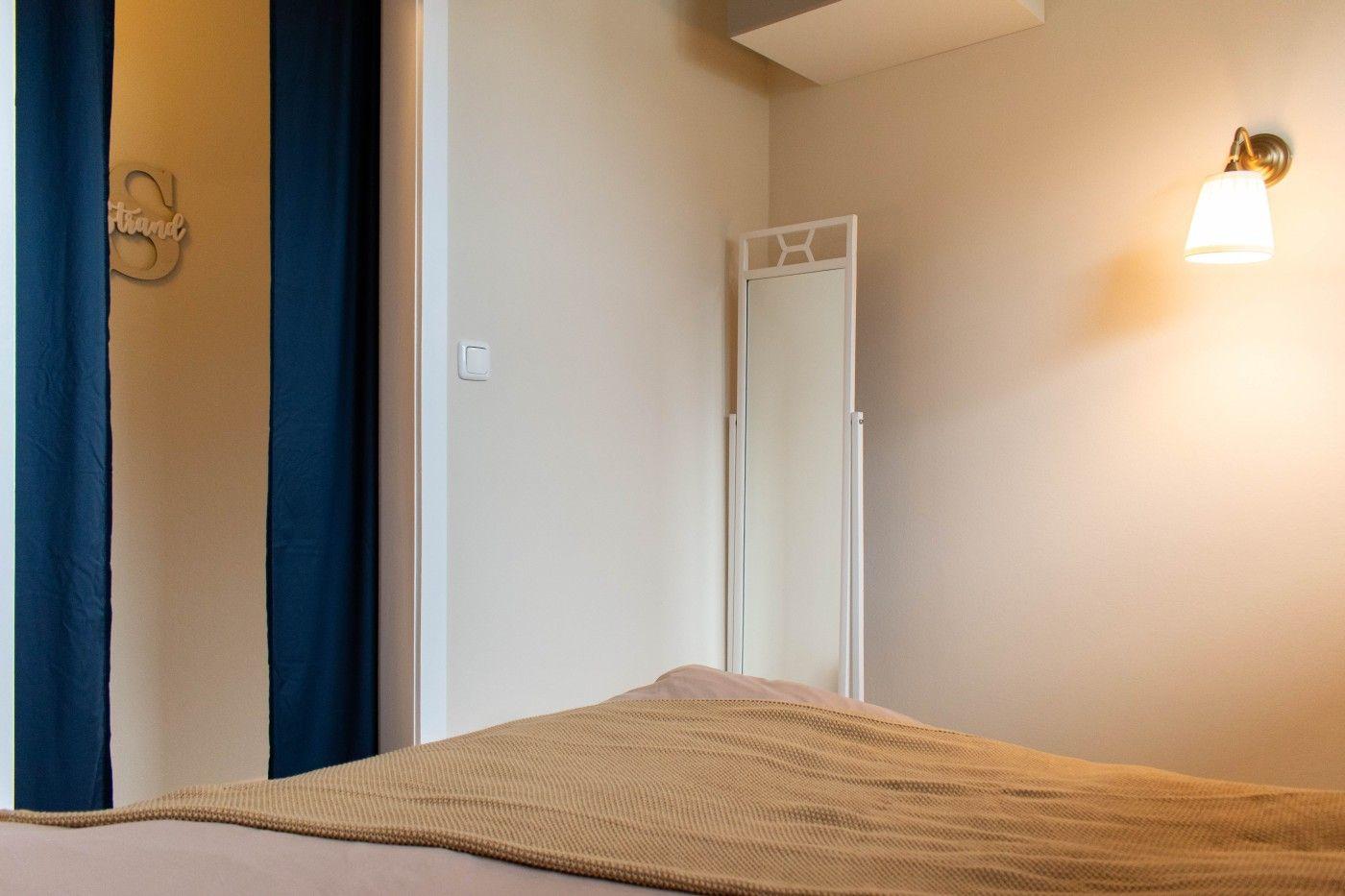 Schlafzimmer mit Bett, Spiegel und Wandlampe. Dunkelblaue Vorhänge und Wanddekoration.