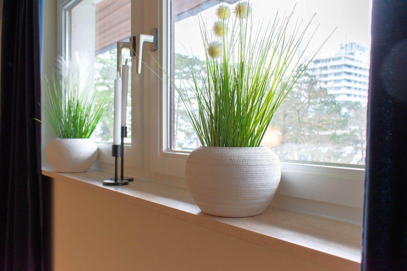 Fensterbank mit zwei Pflanzen in weißen Töpfen und Kerzenhalter.