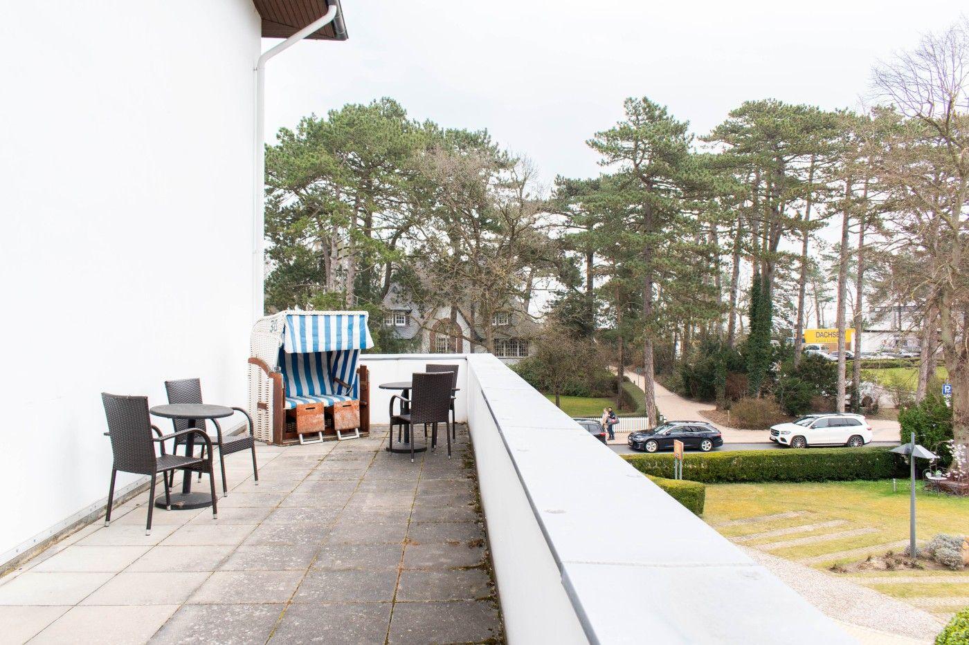 Terrasse mit Tisch, Stühlen und Strandkorb. Blick auf Bäume und Straße.