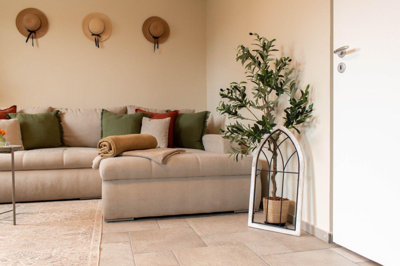 Wohnzimmer mit Sofa, Kissen und Zimmerpflanze in einem weißen Käfig.