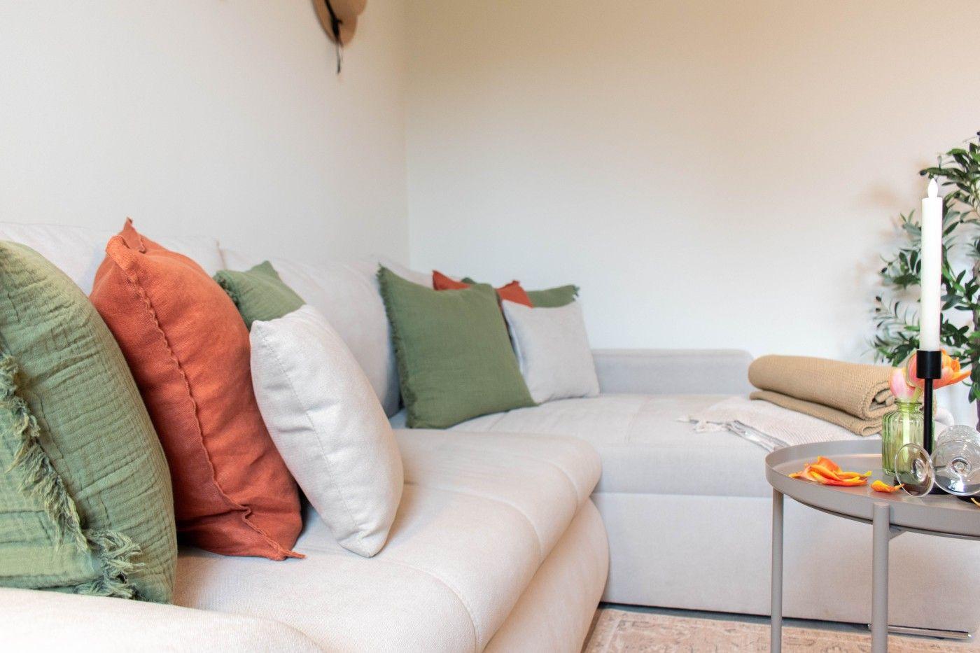 Ein Sofa mit Kissen in Grün und Orange. Tisch mit Kerze und Pflanze.