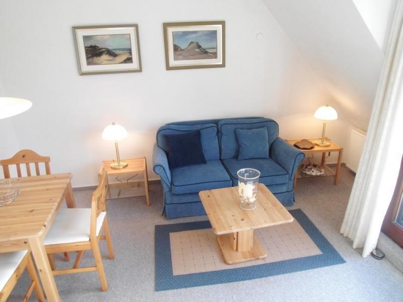 Wohn- und Essbereich mit blauem Sofa, Holztisch und Bildern an der Wand.