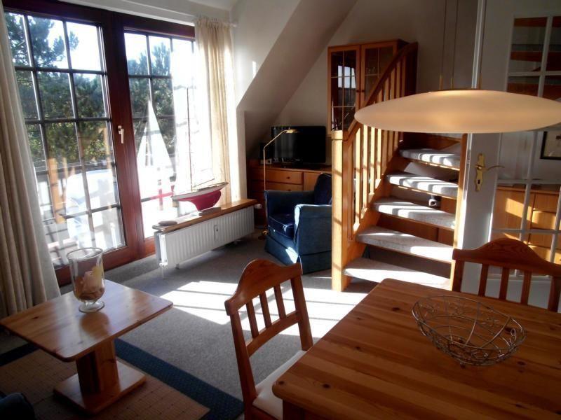 Wohn- und Essbereich mit Holztreppe und großem Fenster. Möbel und Einrichtung sind sichtbar.