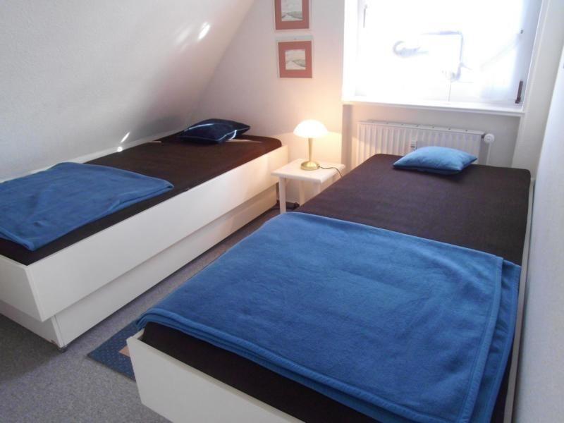 Zwei Einzelbetten mit blauen Decken und Kissen in einem Schlafzimmer mit Fenster und Nachttisch.