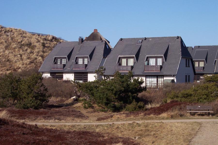 Moderne Ferienhäuser mit Balkonen und dunklen Dächern stehen in einer natürlichen Umgebung.