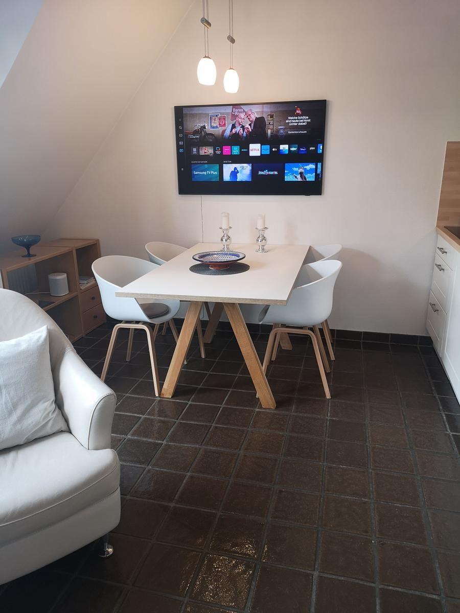 Essbereich mit Tisch, Stühlen und Wand-TV unter schräger Decke.