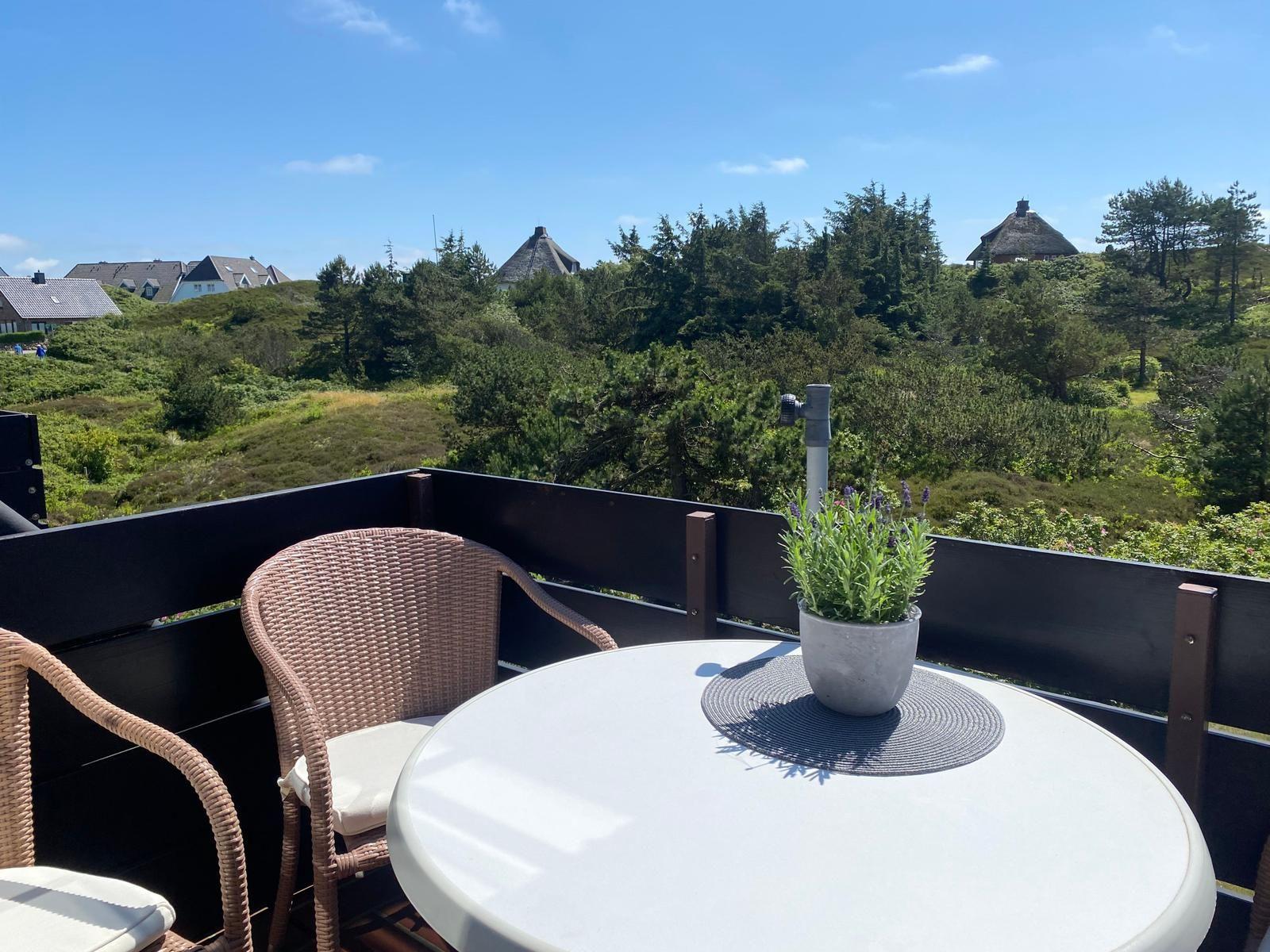 Terrasse mit Tisch, Stühlen und Lavendel. Blick auf grüne Hügel und Häuser.