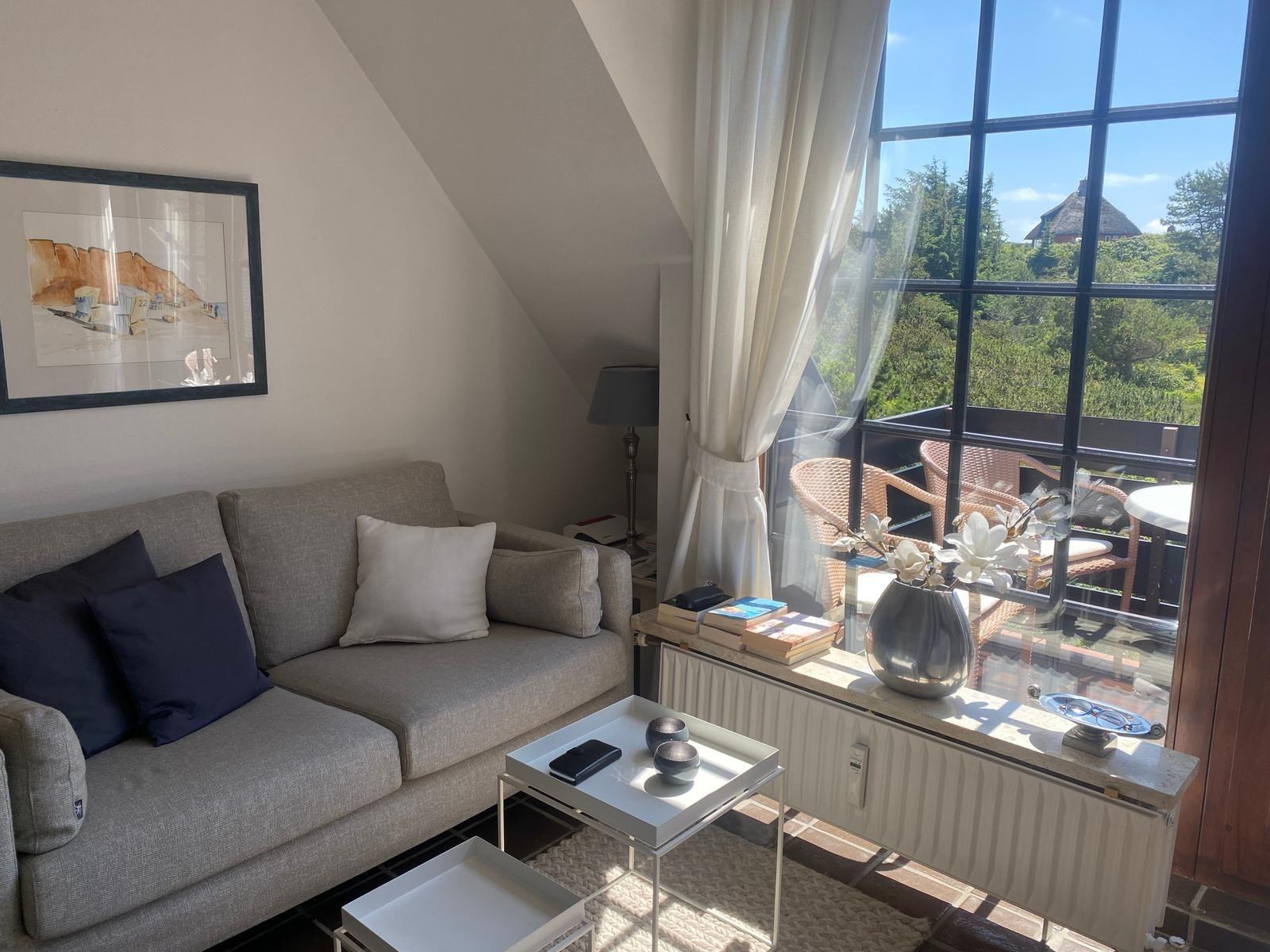 Wohnzimmer mit Sofa, Tisch und Blick auf Balkon mit Garten.