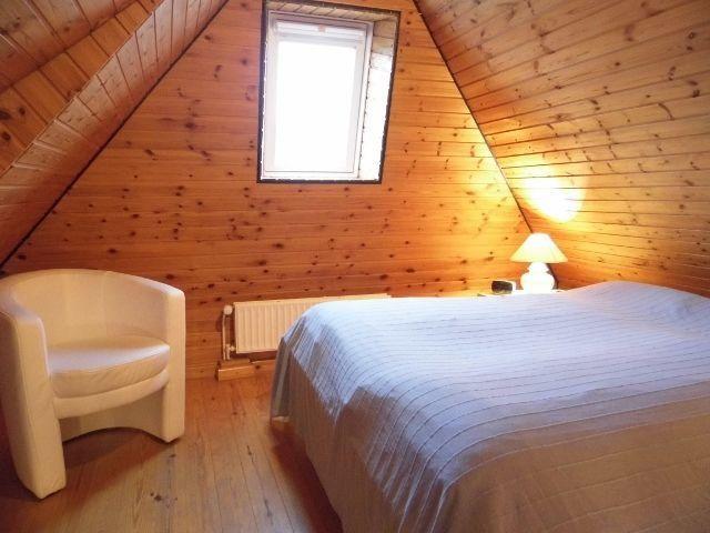 Schlafzimmer mit Bett, Sessel und Fenster unter Holzdecke.