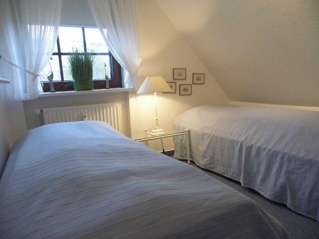 Zwei Betten unter einem Dachbodenfenster mit Vorhängen und einer Stehlampe.